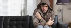 man in coat shivering from cold in his living room
