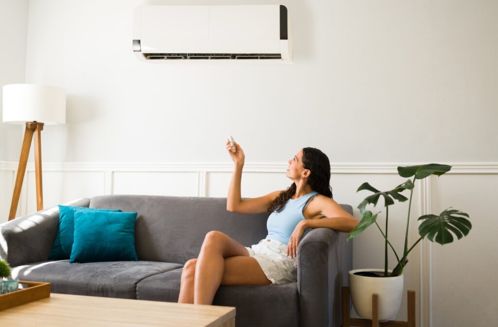 A person sitting on a gray sofa uses a remote to operate a wall-mounted air conditioner in a living room with minimal decor. ac repair beech mountain